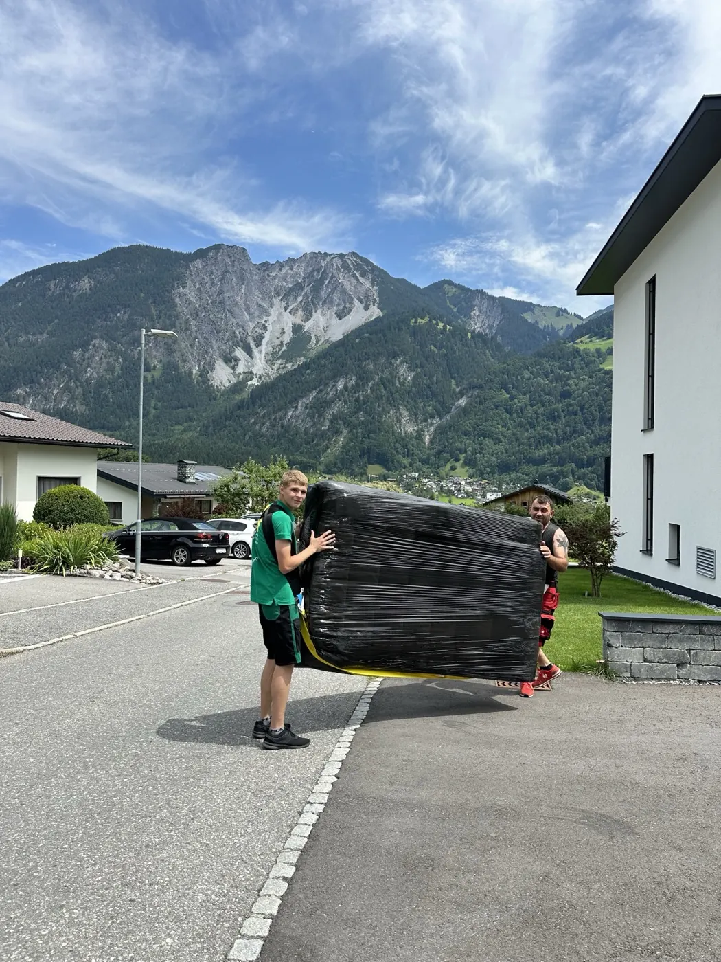 Zwei Mitarbeiter von Umzug Mödling tragen ein verpacktes Möbelstück zum Fahrzeug